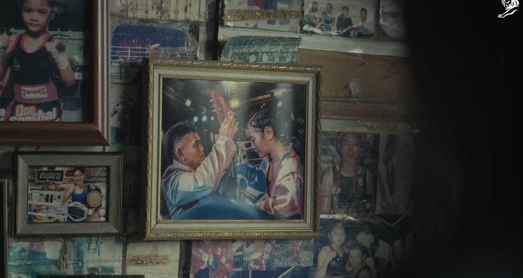 Framed photograph of a boxing trainer blessing a young female boxer before a match, displayed among family photos on a wall.