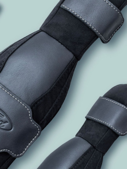 Three Ford SupportBelt™ padded seatbelt covers displayed on a sage green background, showing the black and grey faux leather construction, white contrast stitching, adjustable straps, and embossed Ford logo.