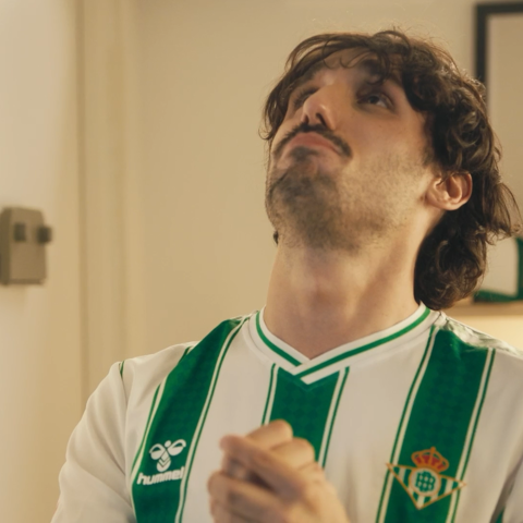 Real Betis supporter wearing the club’s green and white shirt, looking upward with hands clasped in anticipation.