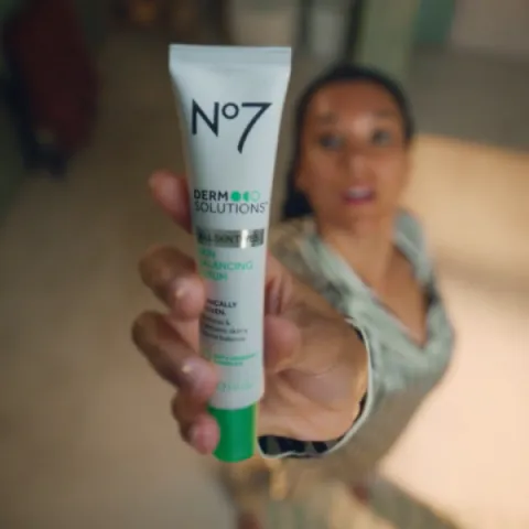 A lady holding up a Boots No7 product to the sky, she is in deep focus and the camera pan in facing down.