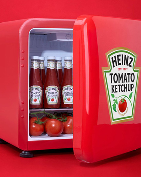 A Heinz ketchup mini-fridge with the door adjar and containing multiple glass bottles of ketchup.