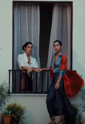 Two women stood by a window with many plant pots hanging on the walls around them.
