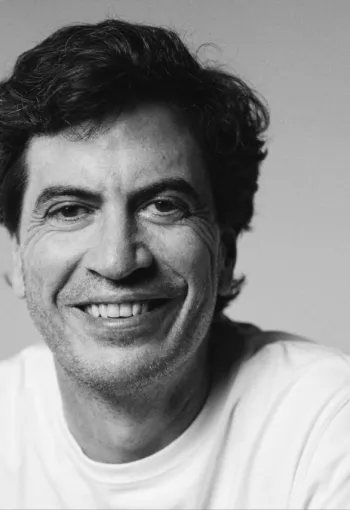 A black and white headshot of a man with dark brown hair smiling into the camera